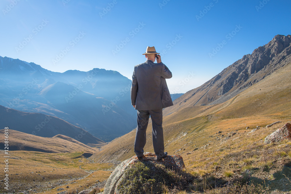 a man in a suit and with a phone in the mountains, panoramic view of the mountains, summer
