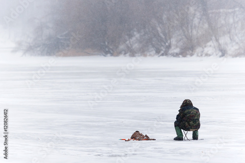 Winter fishing. Man fishes on the ice of a frozen river. Russia.