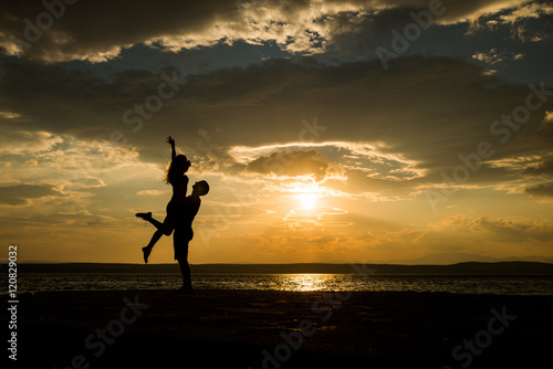 Couple kissing on the beach with a beautiful sunset in background, man lifting the woman