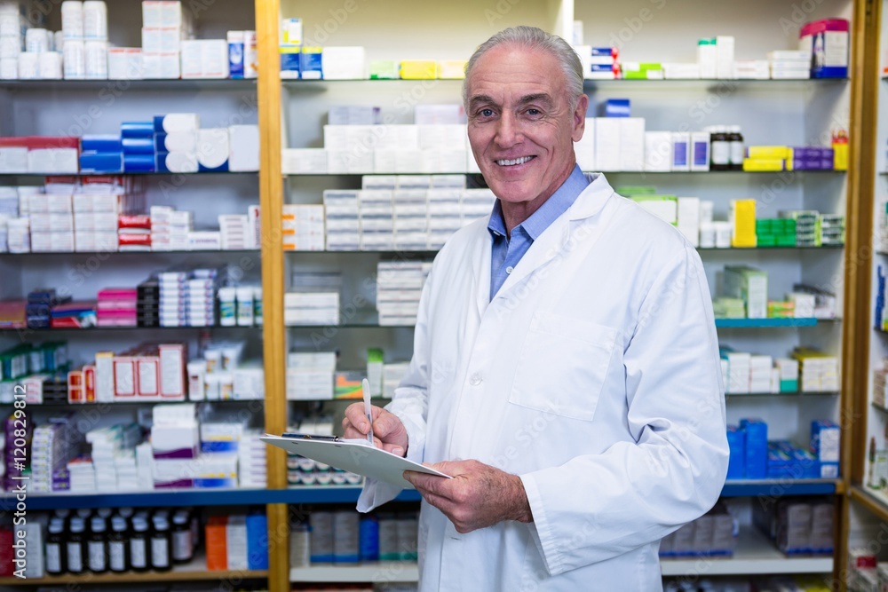 Pharmacist writing on clipboard in pharmacy Pharmacist writing on clipboard in pharmacy