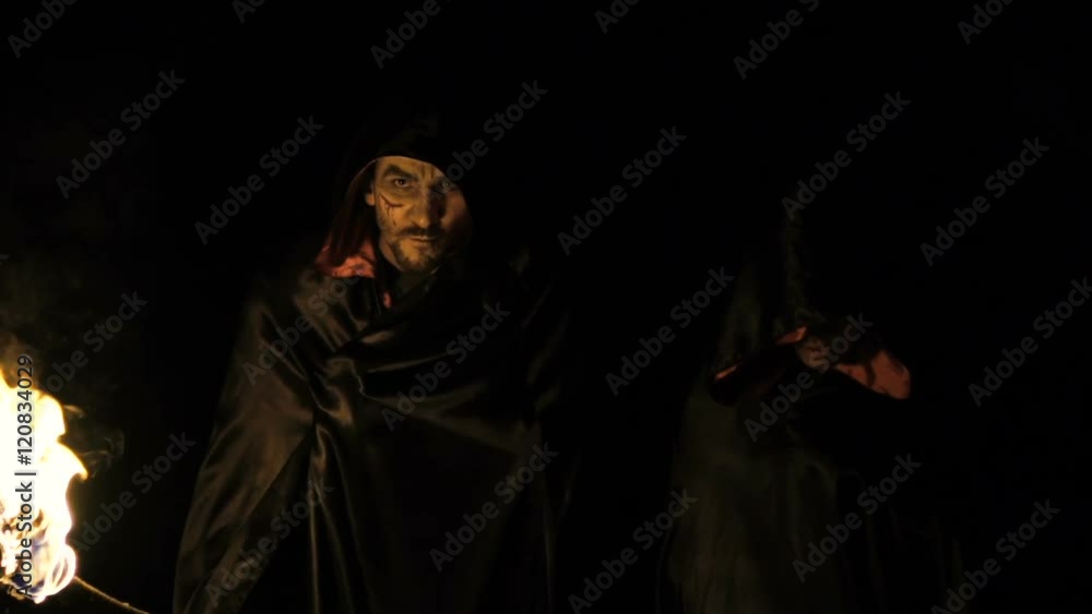 People in black coats with fire in hands going in dark forest. Slowly People in black coats with fire in hands going in dark forest. Slowly