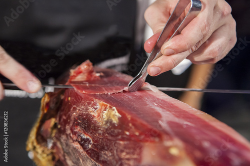Master slicer taking iberian cured ham with tongs
