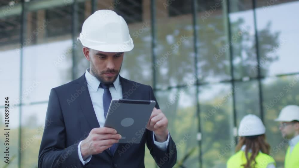 Businessman in Hard Hat Walking, Talking, and Using Tablet Computer. Glass Building or Skyscraper under Construction on Background. Shot on RED Cinema Camera in 4K (UHD). Businessman in Hard Hat Walking, Talking, and Using Tablet Computer. Glass Building or Skyscraper under Construction on Background. Shot on RED Cinema Camera in 4K (UHD).
