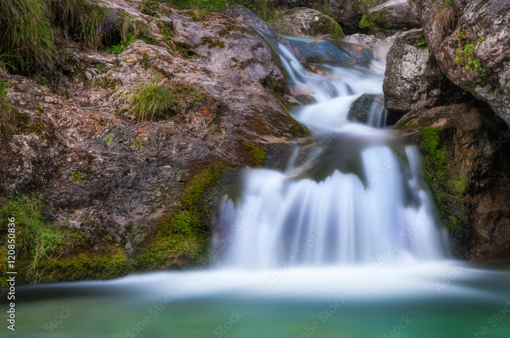 Cascata nella roccia con acque bianche effetto seta che finiscono in  un lago  verde smeraldo