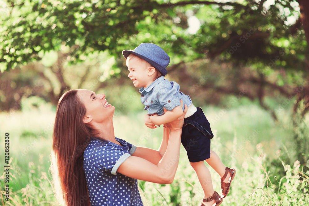 Fototapeta premium Loving mother holding son in her arms, plays with him and hugs him. Family rest on the nature. soft focus