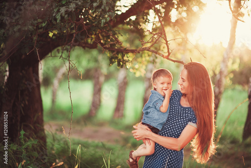 Loving mother holding son in her arms, plays with him and hugs him. Family rest on the nature. soft focus