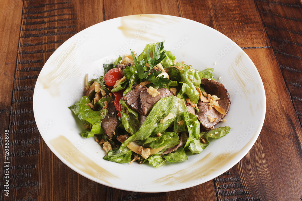 Salad with roast beef in a white plate. Brown wooden background