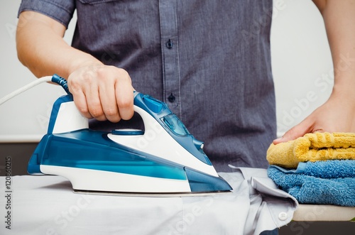 Man irons clothes on ironing board with blue iron