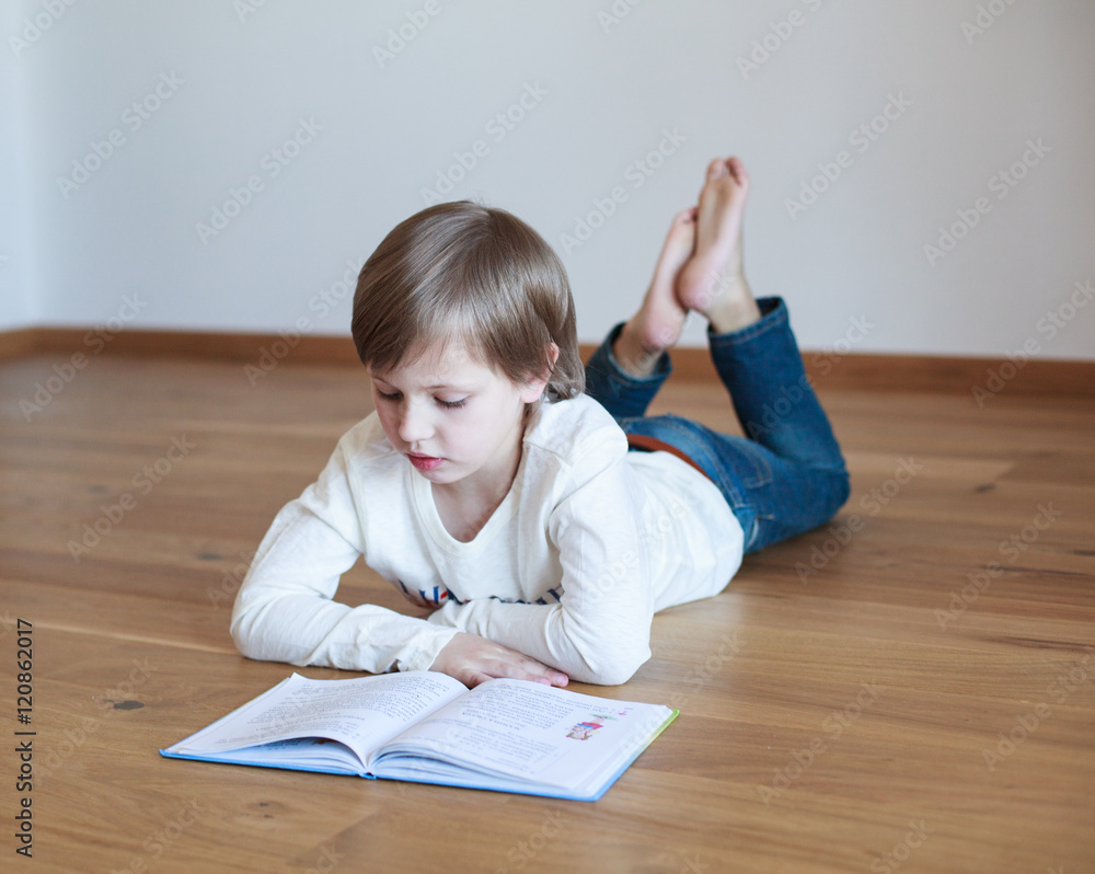 Cute boy doing homework, he is lying on the floor and reading book Cute boy doing homework, he is lying on the floor and reading book