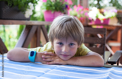 Cute boy with blue smart watch lying on the table at terrace 
