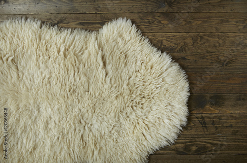 Fotografie An aerial view of a cosy white sheepskin rug on a distressed wooden floor backgr
