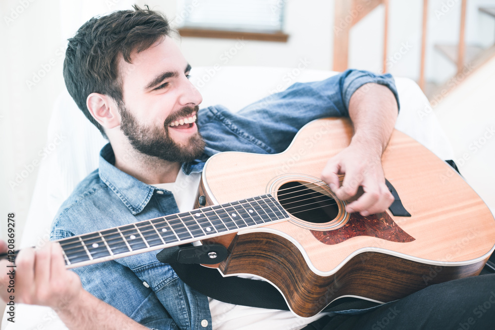 Obraz premium Handsome young man wearing a jeans shirt playing guitar. Music, instrument education, entertainment, pop rock star, music concert and learning concept