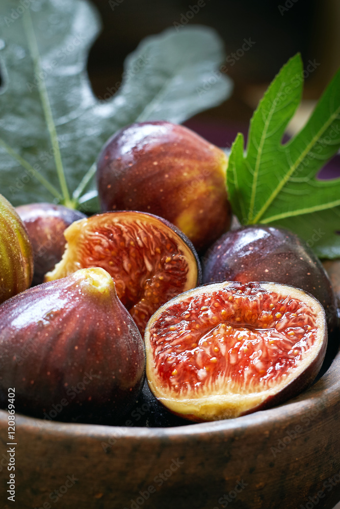 Fototapeta premium Fresh ripe black figs and fig leaves in rustic bowl