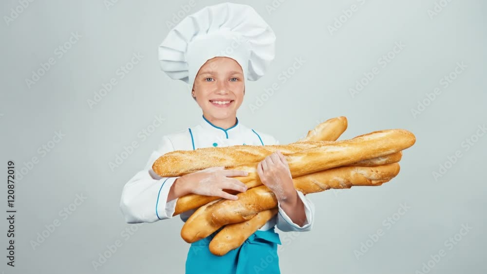 Young baker girl child holds long loaves and smiling at camera. Thumb up. Ok Young baker girl child holds long loaves and smiling at camera. Thumb up. Ok