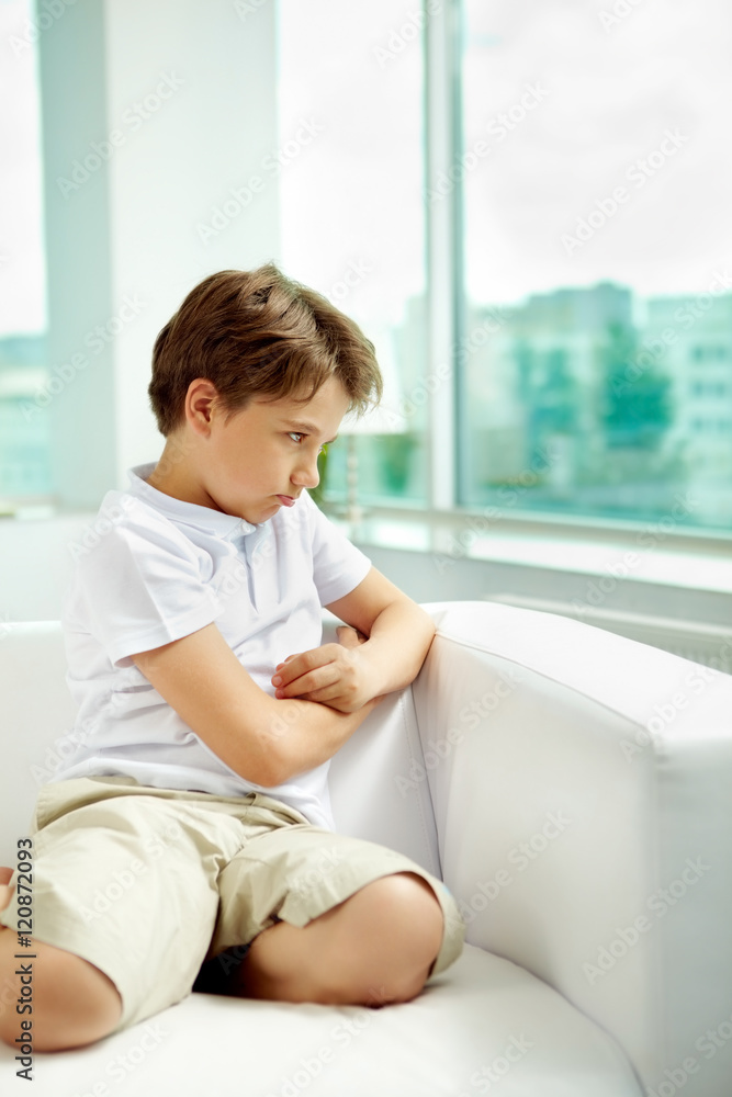 Little sulky boy sitting on sofa Little sulky boy sitting on sofa