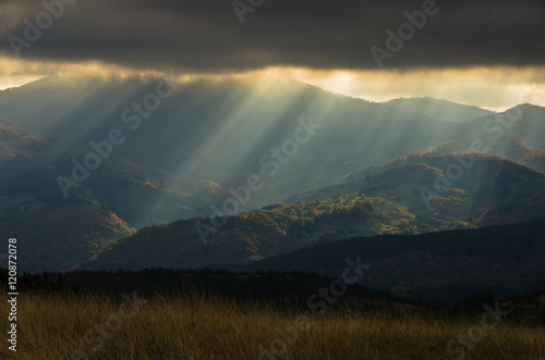 Heavy overcast sky with sunrays over meadows and colorful forests at autumn, mountain Goc, Serbia