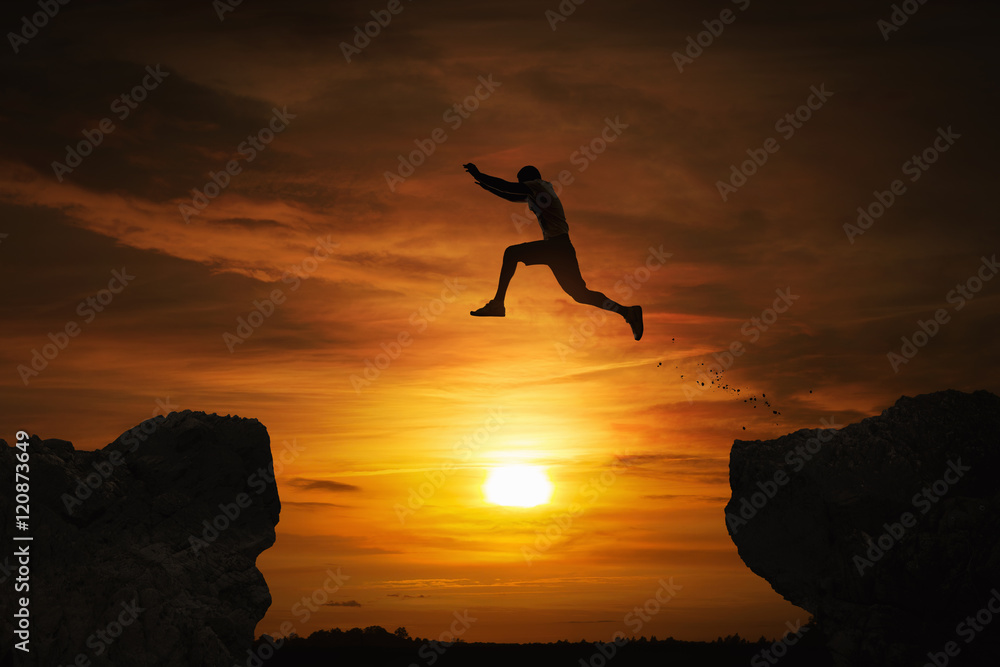Silhouette of a man jumping over abyss at sunset with copy space - obrazy, fototapety, plakaty 