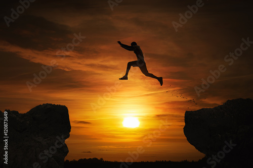 Silhouette of a man jumping over abyss at sunset with copy space