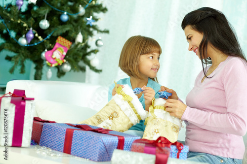 Mother and daughter sitting at Christmas tree and examining their presents