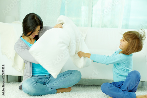 Mother and her little daughter fighting with pillows at home