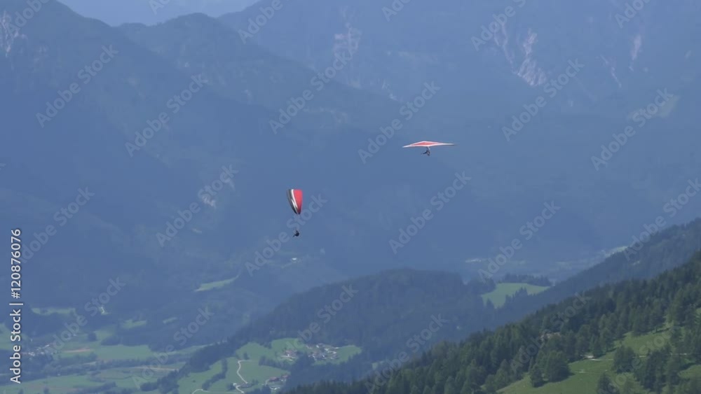 Red hang glider and red paraglider fly together
