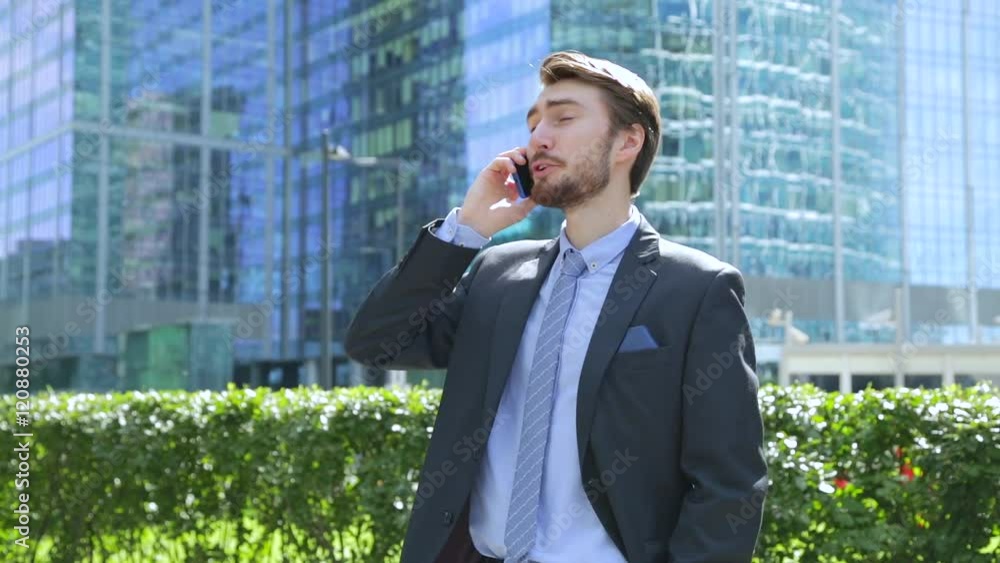 Handsome businessman is talking on the phone near the modern business center, skyscraper (slider shot) Handsome businessman is talking on the phone near the modern business center, skyscraper (slider shot)