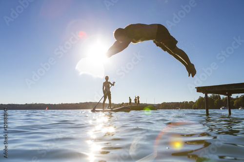 Mann springt vom Steg in den See