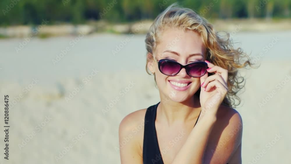 Beautiful young woman smiling at the camera, looking over sunglasses. On the beach on a sunny day Beautiful young woman smiling at the camera, looking over sunglasses. On the beach on a sunny day