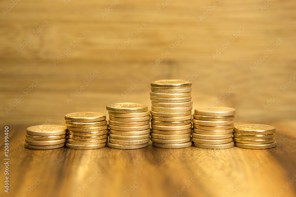 Golden coins piles up and down on wooden background. Selective focus. Golden coins piles up and down on wooden background. Selective focus.