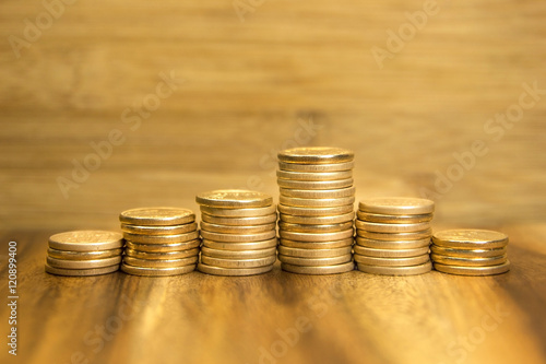 Golden coins piles up and down on wooden background. Selective focus.