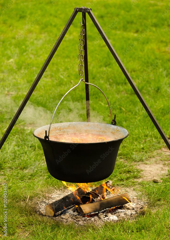 Stew cooking in kettle on tripod on spring meadow Stew cooking in kettle on tripod on spring meadow