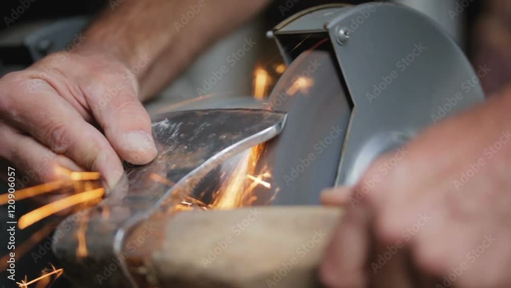 The man sharpens ax on a special machine. Old ax. The man sharpens ax on a special machine. Old ax.