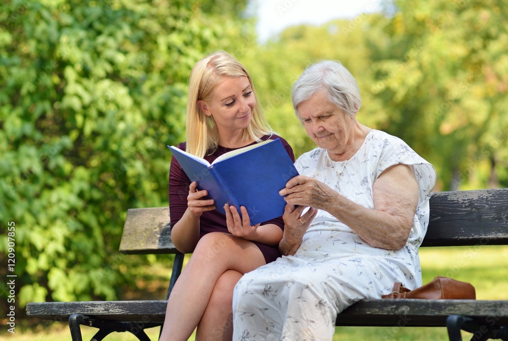 Young woman reading a book elderly woman in the park.