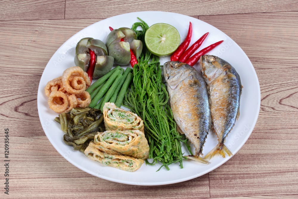 Ready side dish of deep fired mackarel,vegetable omelet,crispy pork rind,pickle lettuce,halve green lemon,red chili and boiled of eggplant,lentils,acacia on wood. Side view Ready side dish of deep fired mackarel,vegetable omelet,crispy pork rind,pickle lettuce,halve green lemon,red chili and boiled of eggplant,lentils,acacia on wood. Side view