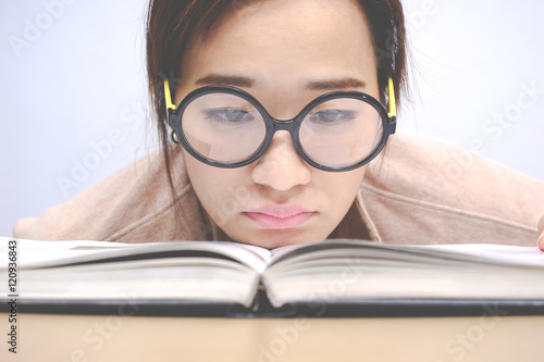 Nerdy young asian woman student with old big round glasses bored with reading book