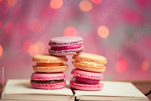 Homemade macaroons stay on open book over christmas lights. Selective focus.
