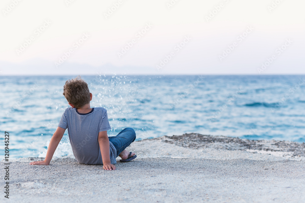Child enjoying the sunset seascape sitting on a pier