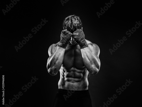 Unrecognizable topless man in fighting gloves covering face with fists on black background. Isolate.