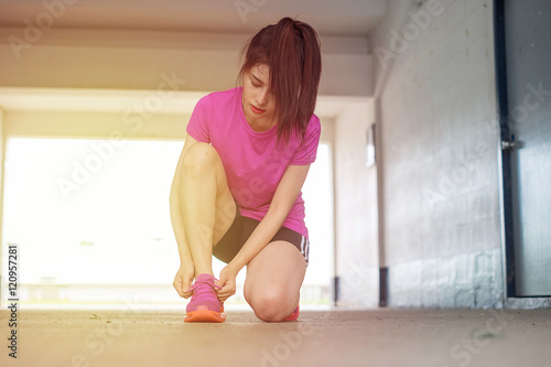 Cropped shot view of young fit woman tie shoelaces while standing on a road during jogging in summer evening, sporty girl tying the laces on running shoes