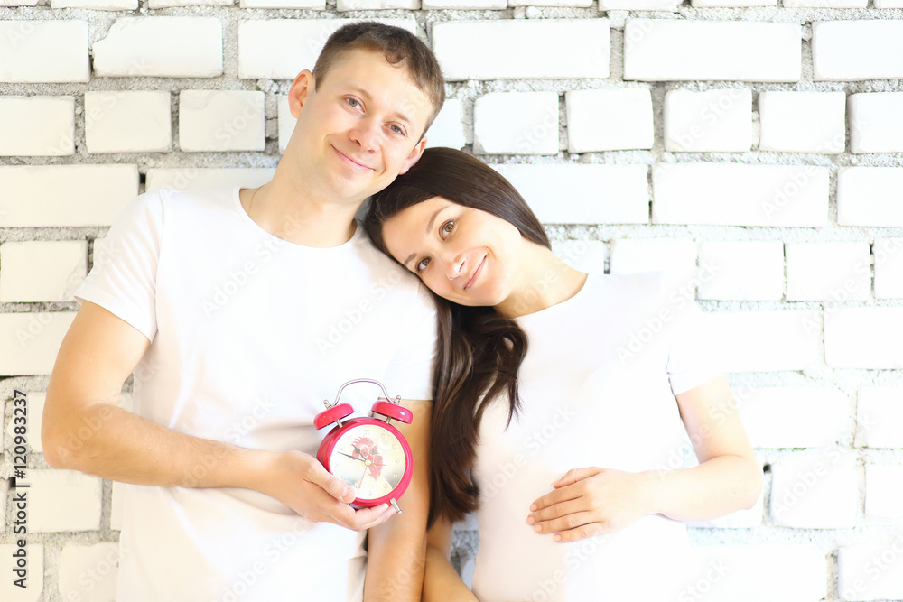 Young pregnant woman and her husband with red alarm clock Young pregnant woman and her husband with red alarm clock