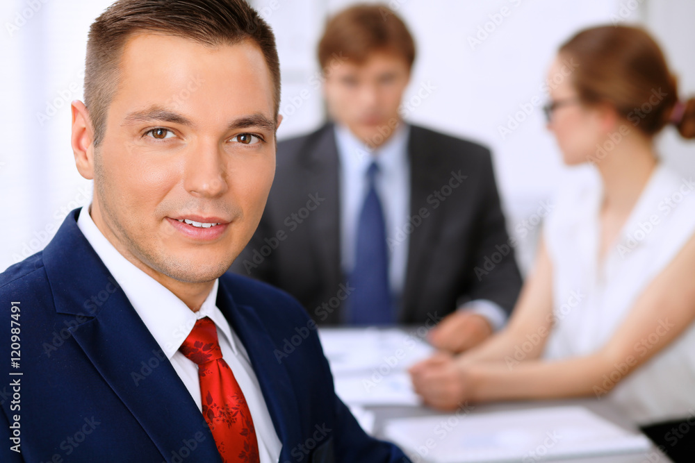 Portrait of cheerful smiling business man against a group of business people at a meeting. Portrait of cheerful smiling business man against a group of business people at a meeting.