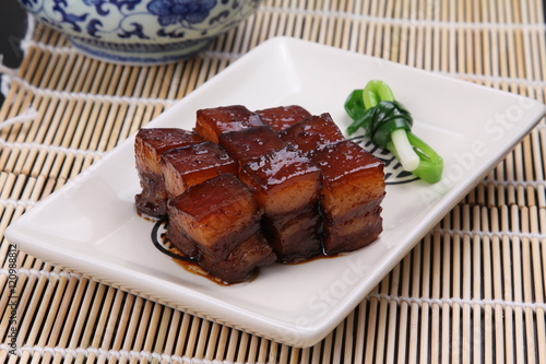 Stewed pork meat in chinese style on white plate on bamboo tray