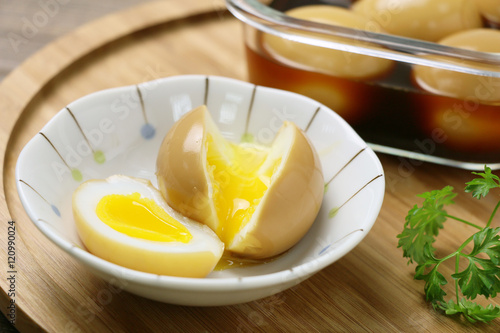 Runny eggs on white bowl with braised eggs on wooden table
