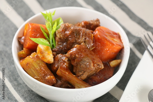 Stewed beef with carrot, garlic and herbs in white bowl on the t