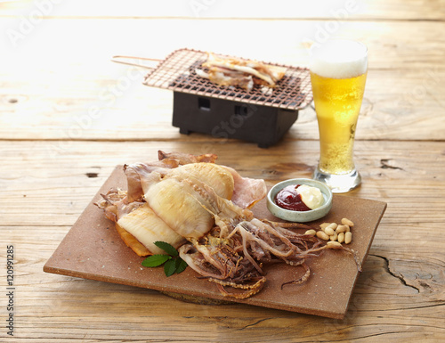 Dried squid with sauces, beer and hot grill on wooden background