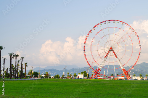 ferris wheel on green field, mountains, palms and blue sky with light clouds in Batumi, Georgia