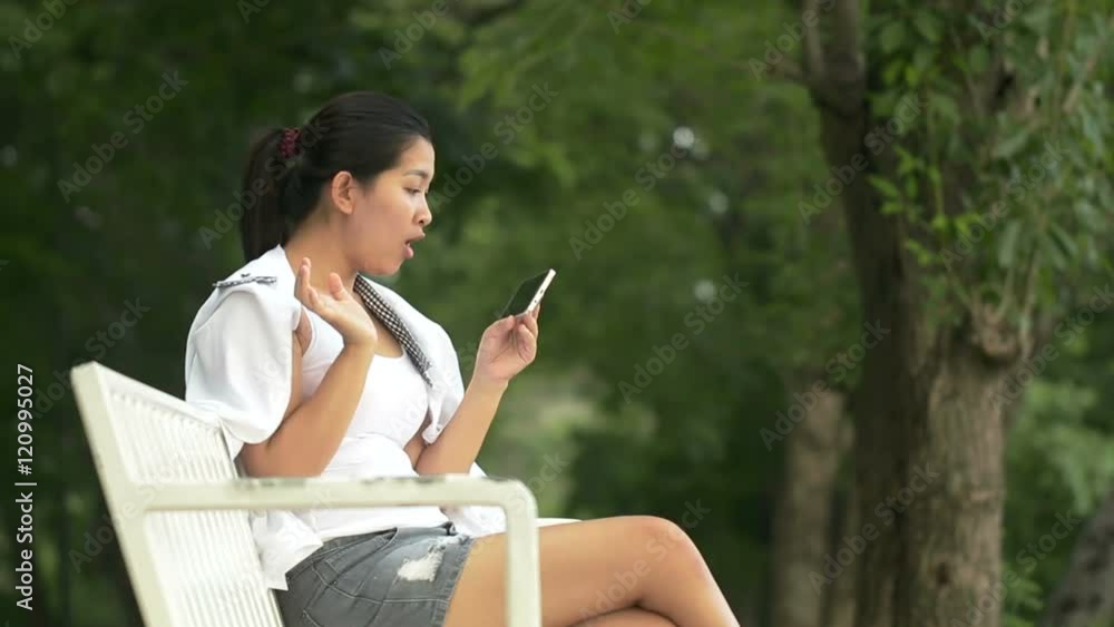 Young asian woman using smartphone and look like relaxing in outdoors looking happy and smiling:Full HD Young asian woman using smartphone and look like relaxing in outdoors looking happy and smiling:Full HD