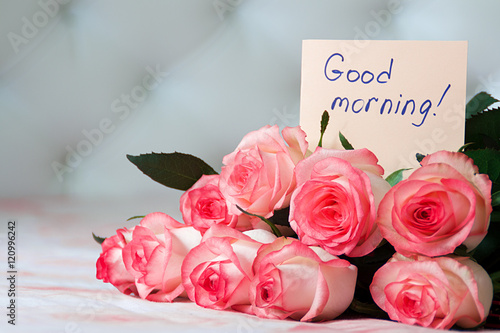 Beautiful bouquet of roses on the bed with message on paper "Good morning". Blurred background