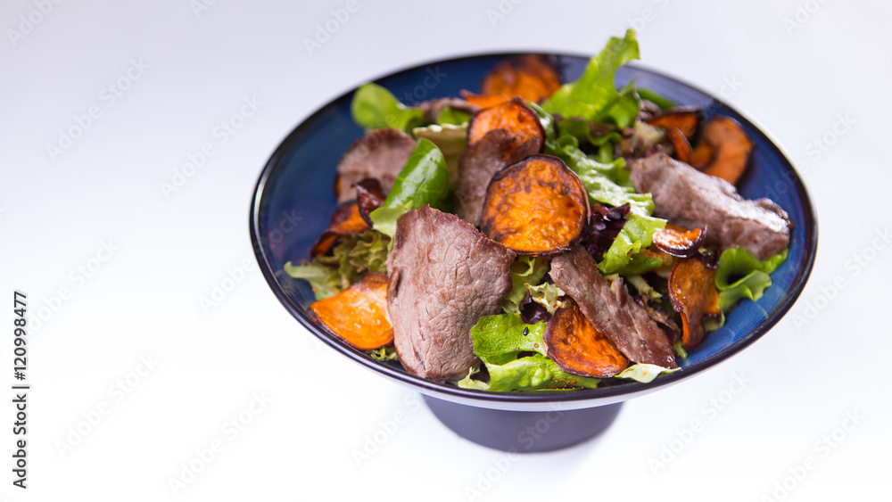 Beef salad with sweet potatoes in blue chinese bowl on white bac