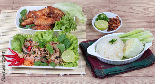 Sticky rice served with fried chicken and spicy sour mixed herb salad of chicken and liver chicken on wood. Top view.